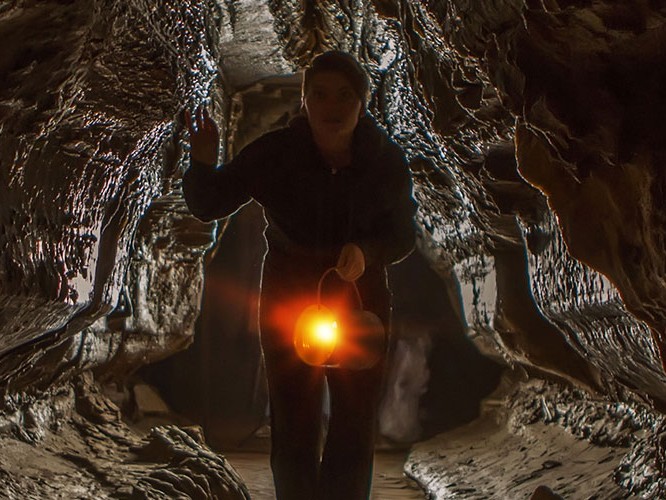 A visitor carrying a glowing lantern through a narrow, sculpted limestone passage